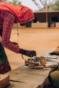 A local chef serving a traditional Rajasthani farm-to-table meal in handcrafted brass utensils at Anopura Jaipur, surrounded by the peaceful countryside.